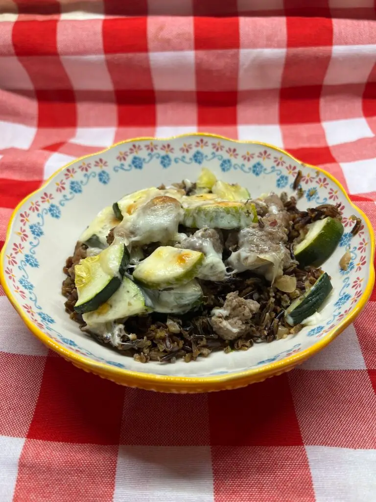 Sausage and zucchini wild rice bake in a white floral dish on a red checked table cl
